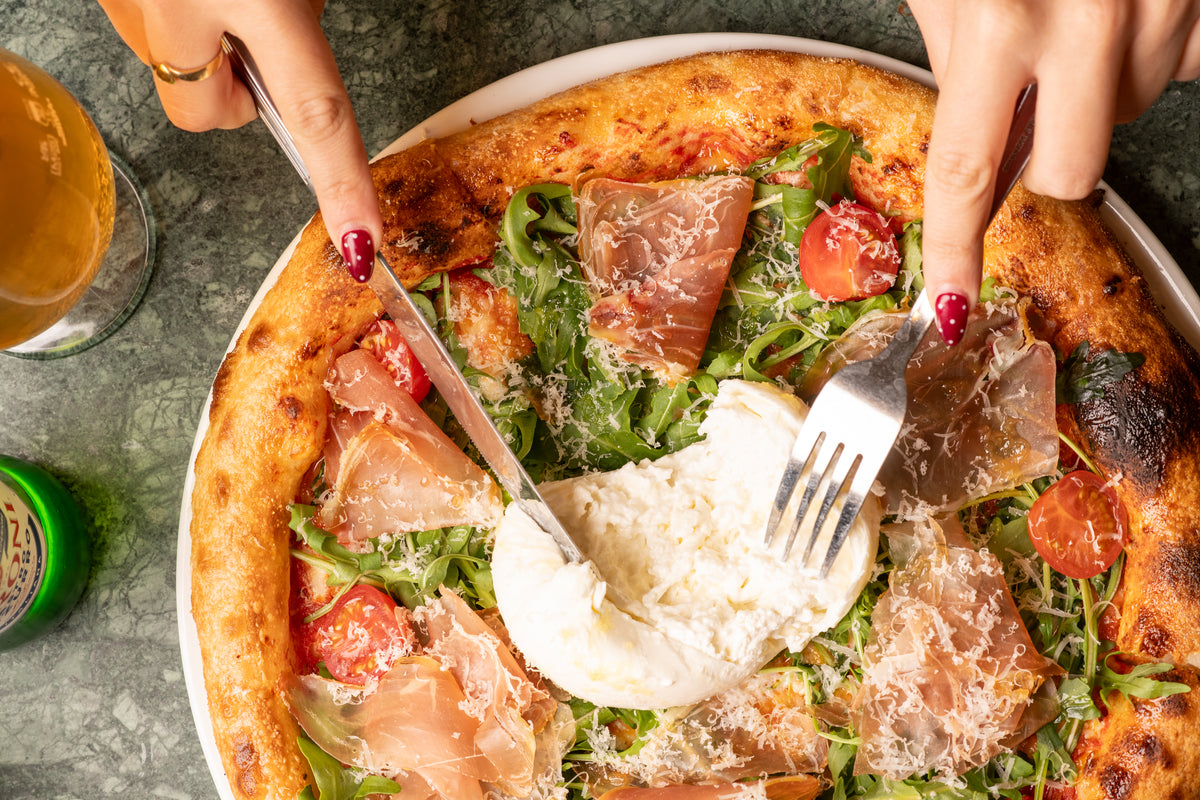 Cutting into a prosciutto and burrata pizza with a cold beer at Fiena, King's Cross